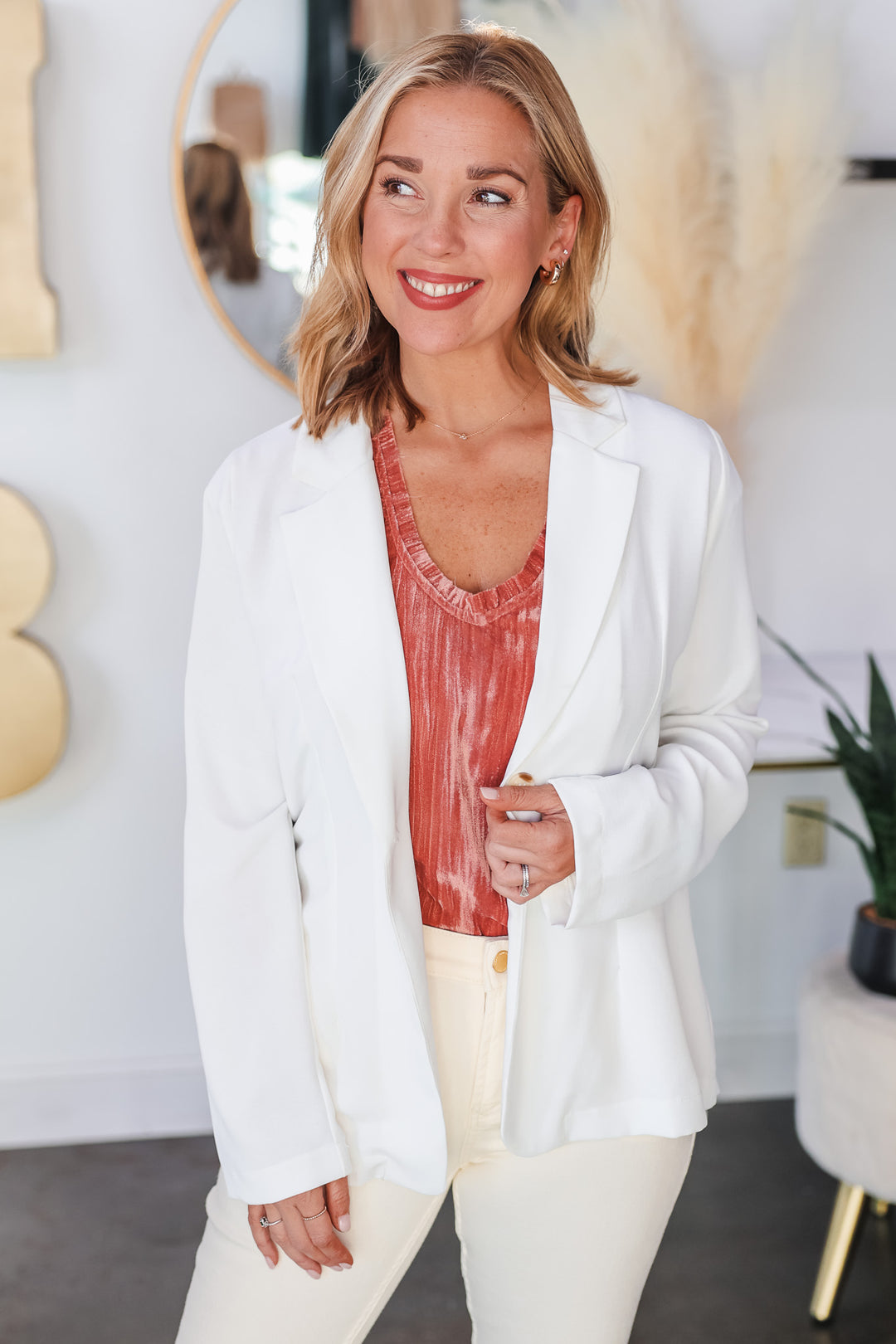 A blonde woman wearing a white lightweight blazer with a rose colored top and wheat colored jeans.