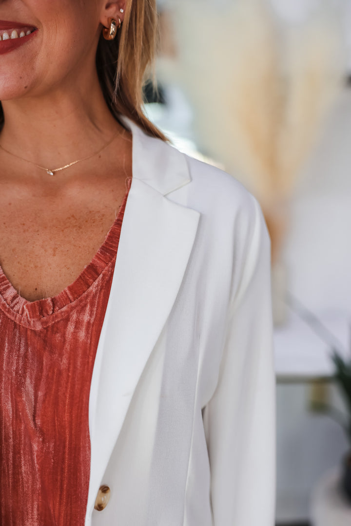 A closeup of a woman wearing a white lightweight blazer and a rose colored top.