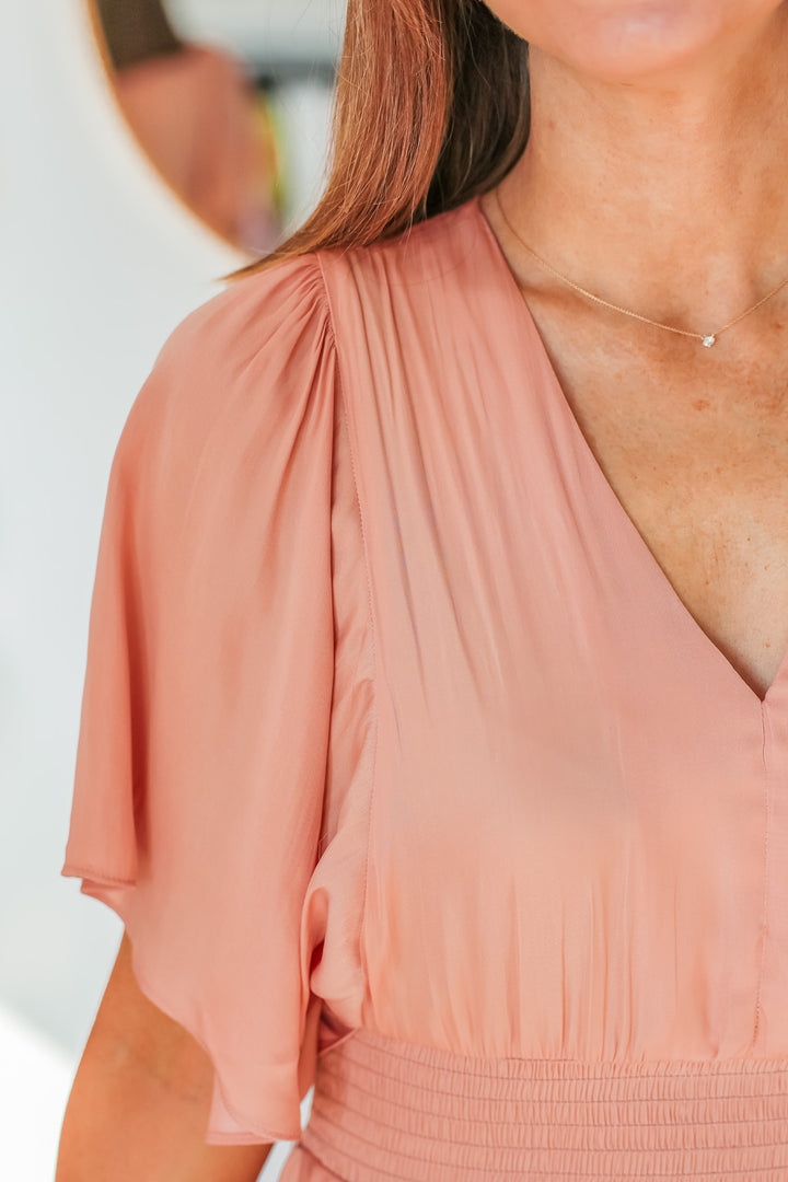 A closeup of the flowy short sleeve and v neck collar of a peach colored dress.