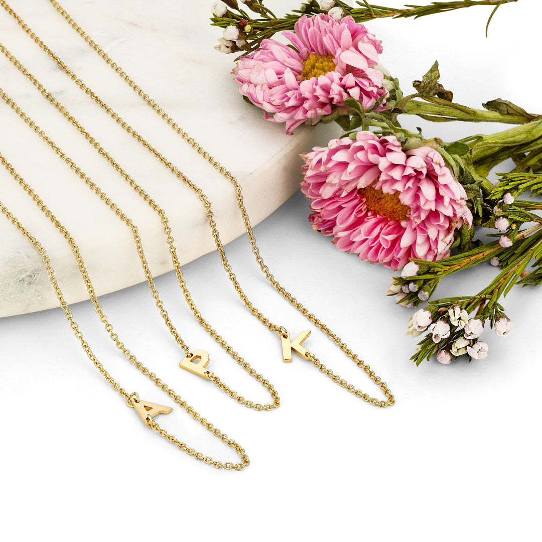 Three gold necklaces lay on a white background with pink flowers on the side.