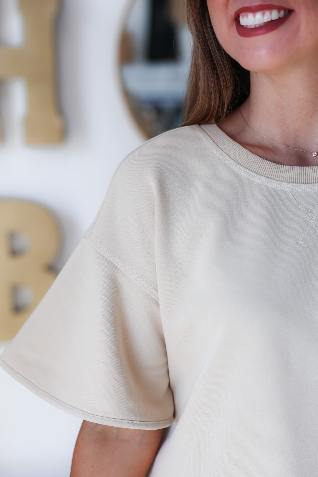 A closeup of the shoulder of a woman wearing a short sleeve tan colored sweatshirt.