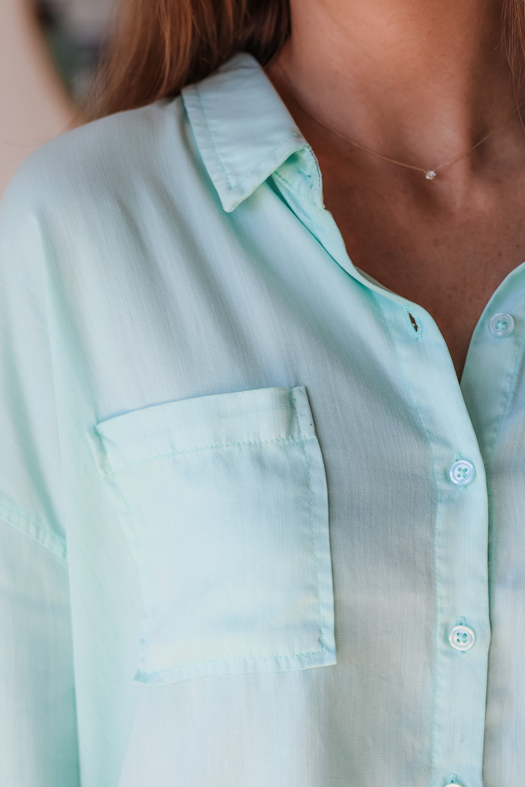 A closeup of the shoulder of a woman wearing a mint green button down with pockets.