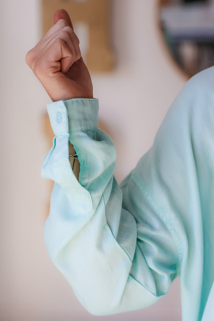 A closeup of the cuff of a mint green button down top.