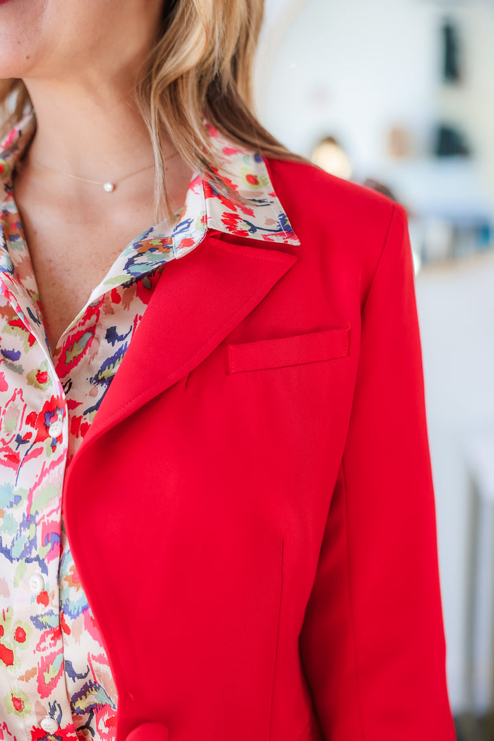 A closeup of the shoulder of a woman wearing a printed blouse with a red blazer.