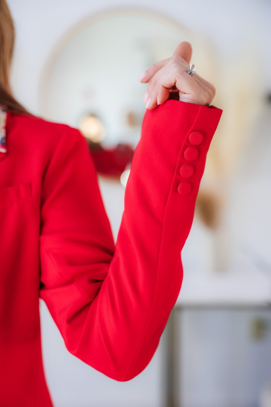A closeup of the cuff of a red blazer with 4 fabric covered buttons.