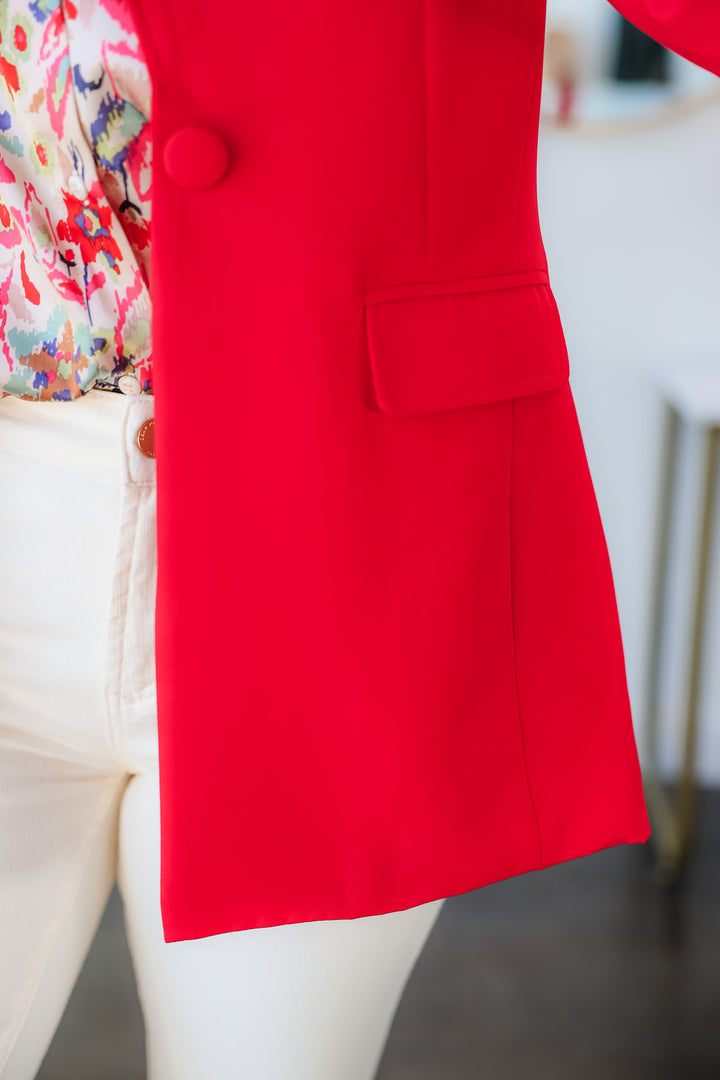 A closeup of the pocket, covered button and hem of the red blazer.