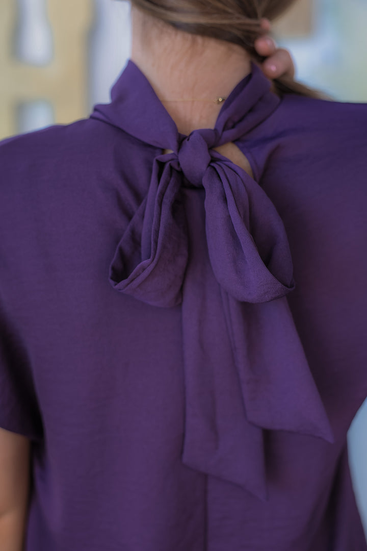 A closeup of a purple tie back blouse with the sashes tied into a bow.