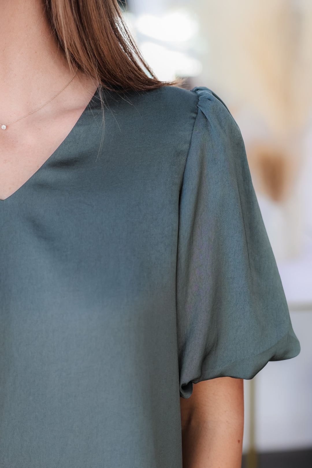 A closeup of the shoulder of a woman wearing an ash green, v neck, short bubble sleeve top.