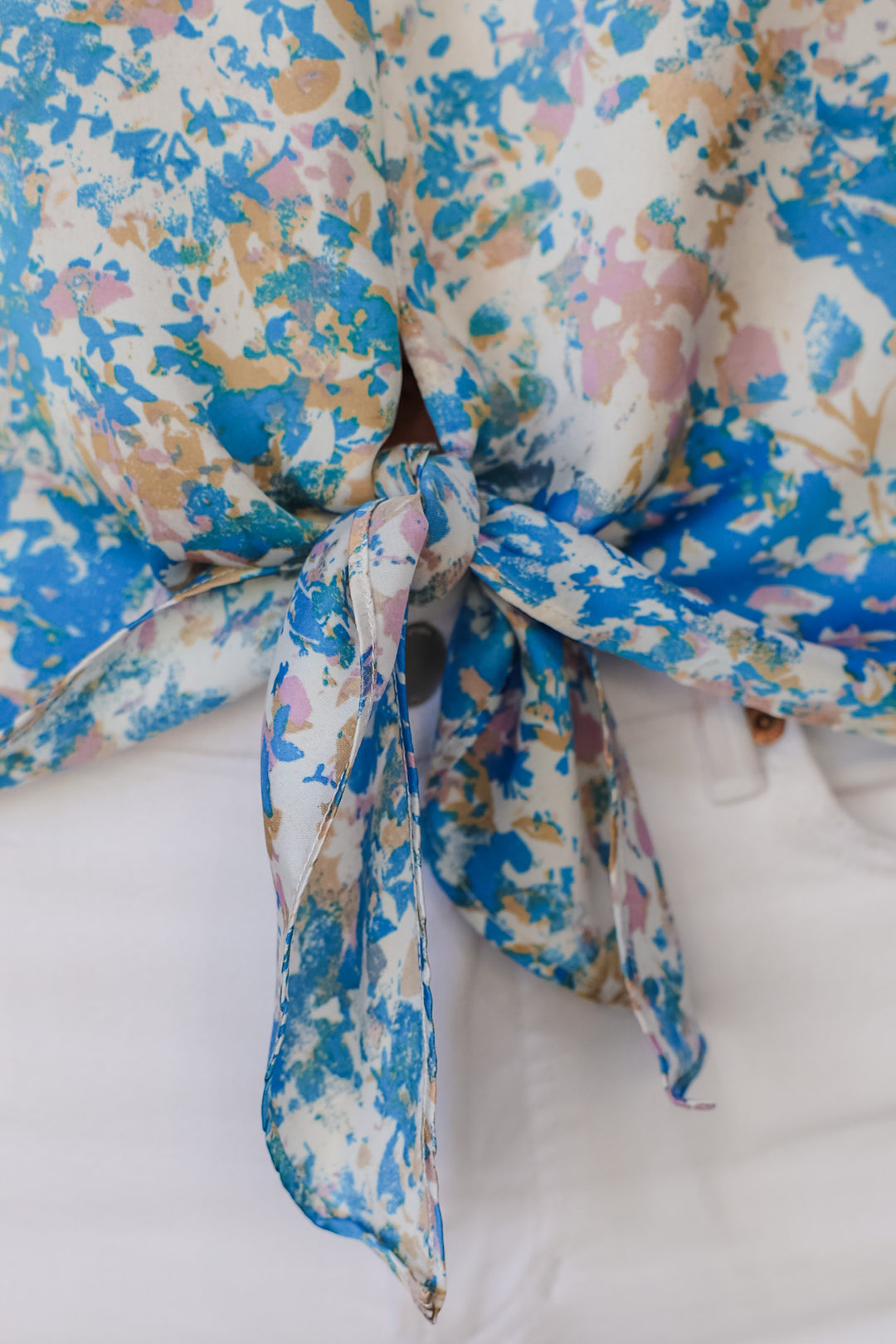 A closeup of the tie on the blue, pink, white, yellow and cream top.
