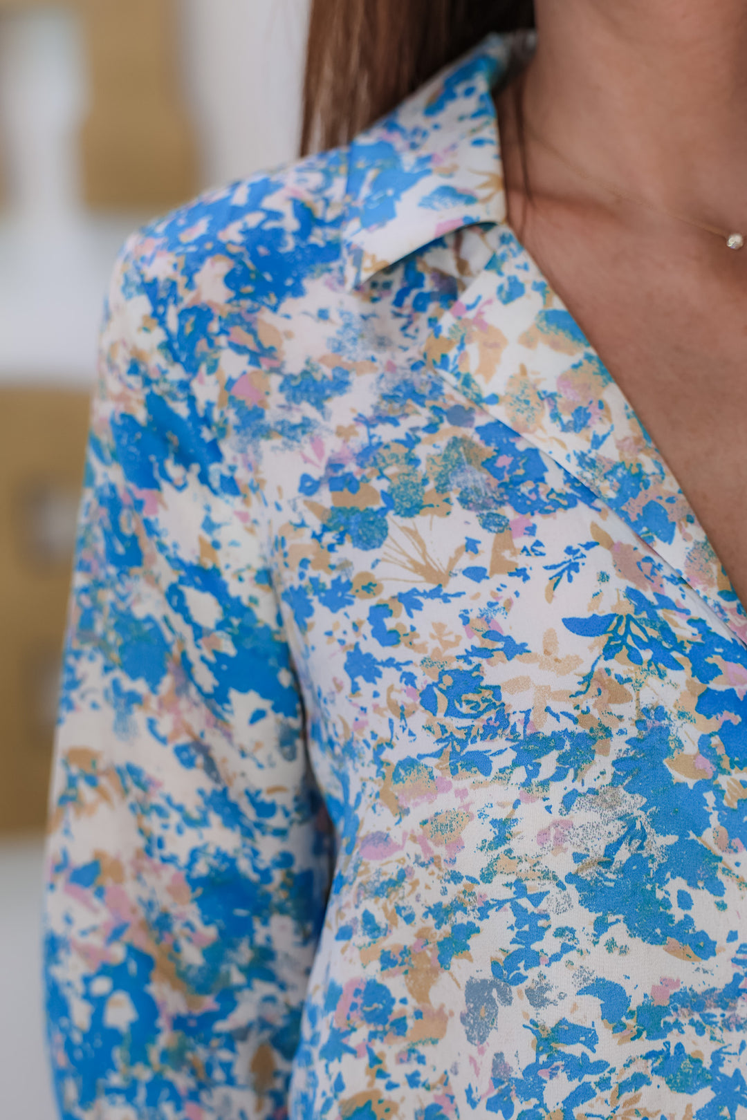 A closeup of the shoulder of a woman wearing a satin top with blue, pink, white, yellow and cream in it.