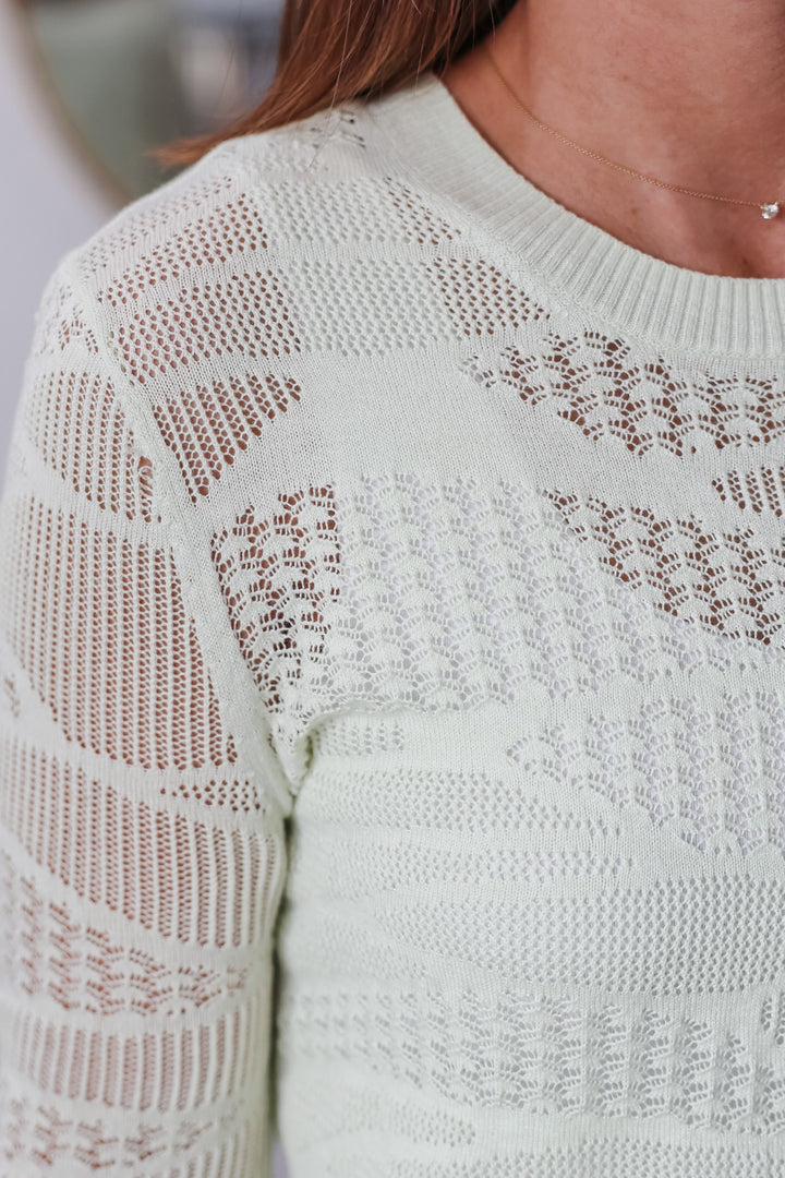 A closeup of the shoulder of a woman wearing a mint green knit top.
