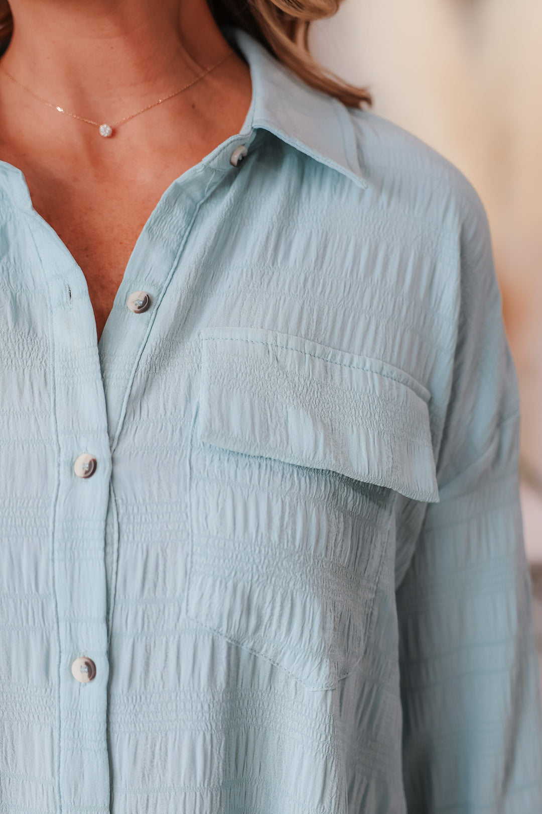 A closeup of the shoulder of a woman wearing a light blue button down dress with a pocket.