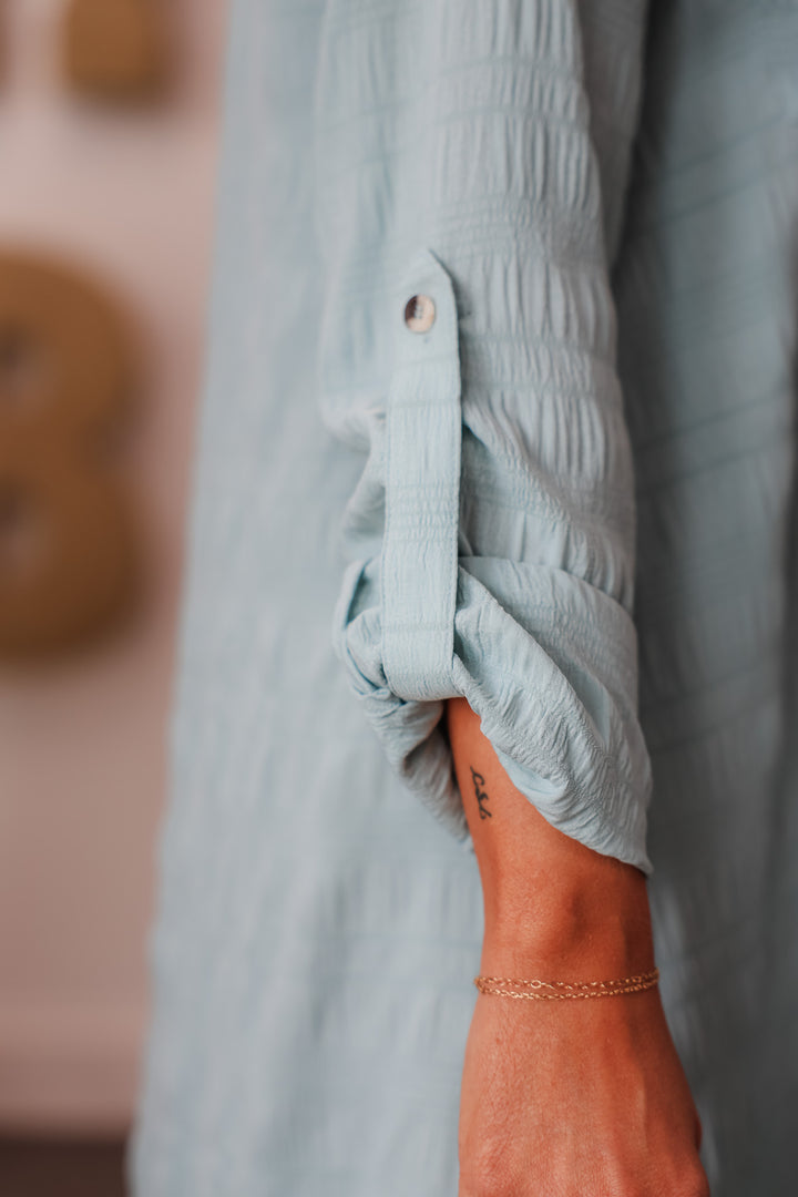 A closeup of the tab sleeve on a light blue button down dress.