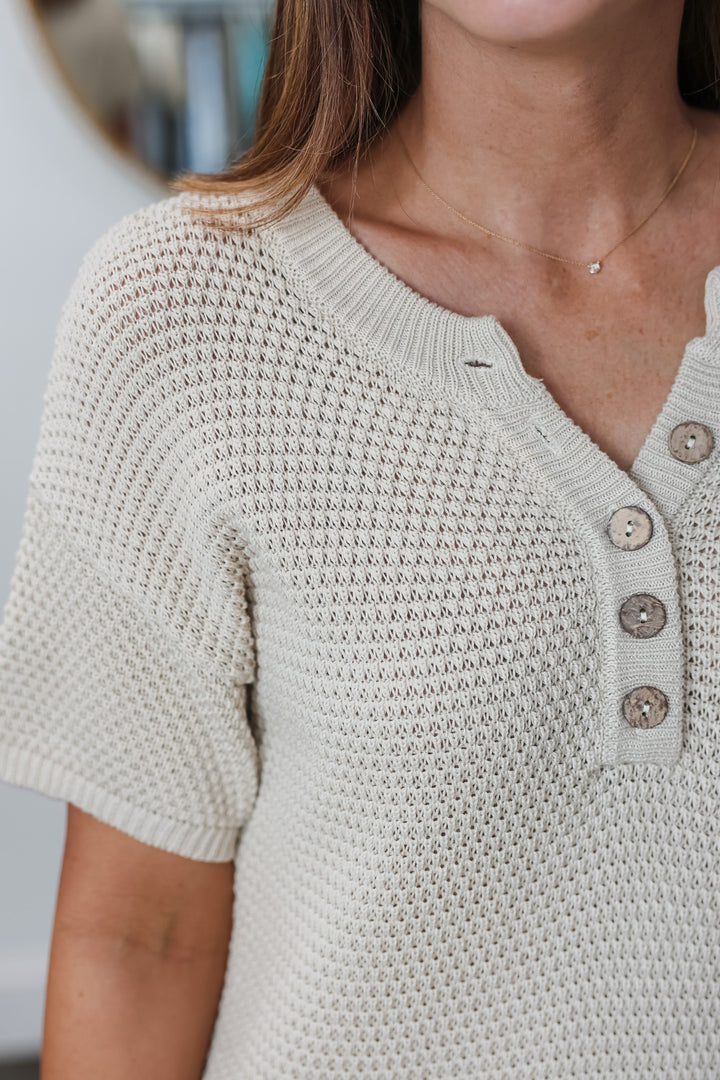 A closeup of the shoulder of a woman wearing a natural colored knit dress with 5 button collar.
