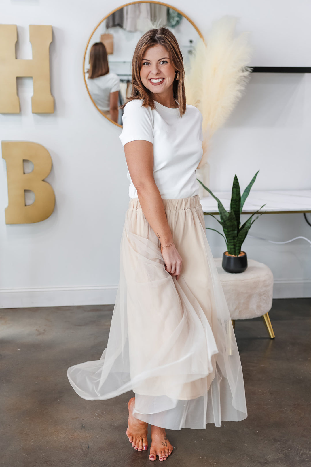 A brunette woman standing in a shop wearing a champagne colored tulle skirt with a basic white tee.