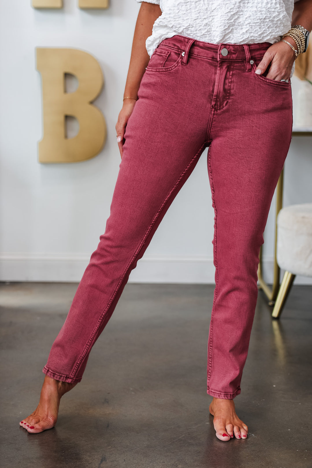 A woman standing in a shop wearing ruby colored jeans with a medium rise and straight leg.