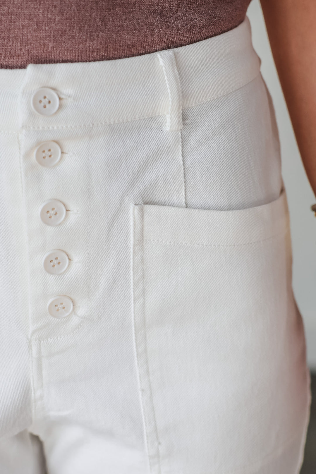 A closeup of the button closure and pockets on white cotton twill pants.
