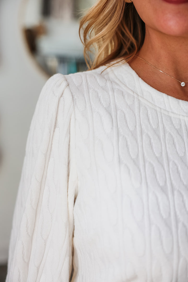 A closeup of the cable knit pattern on a white top.