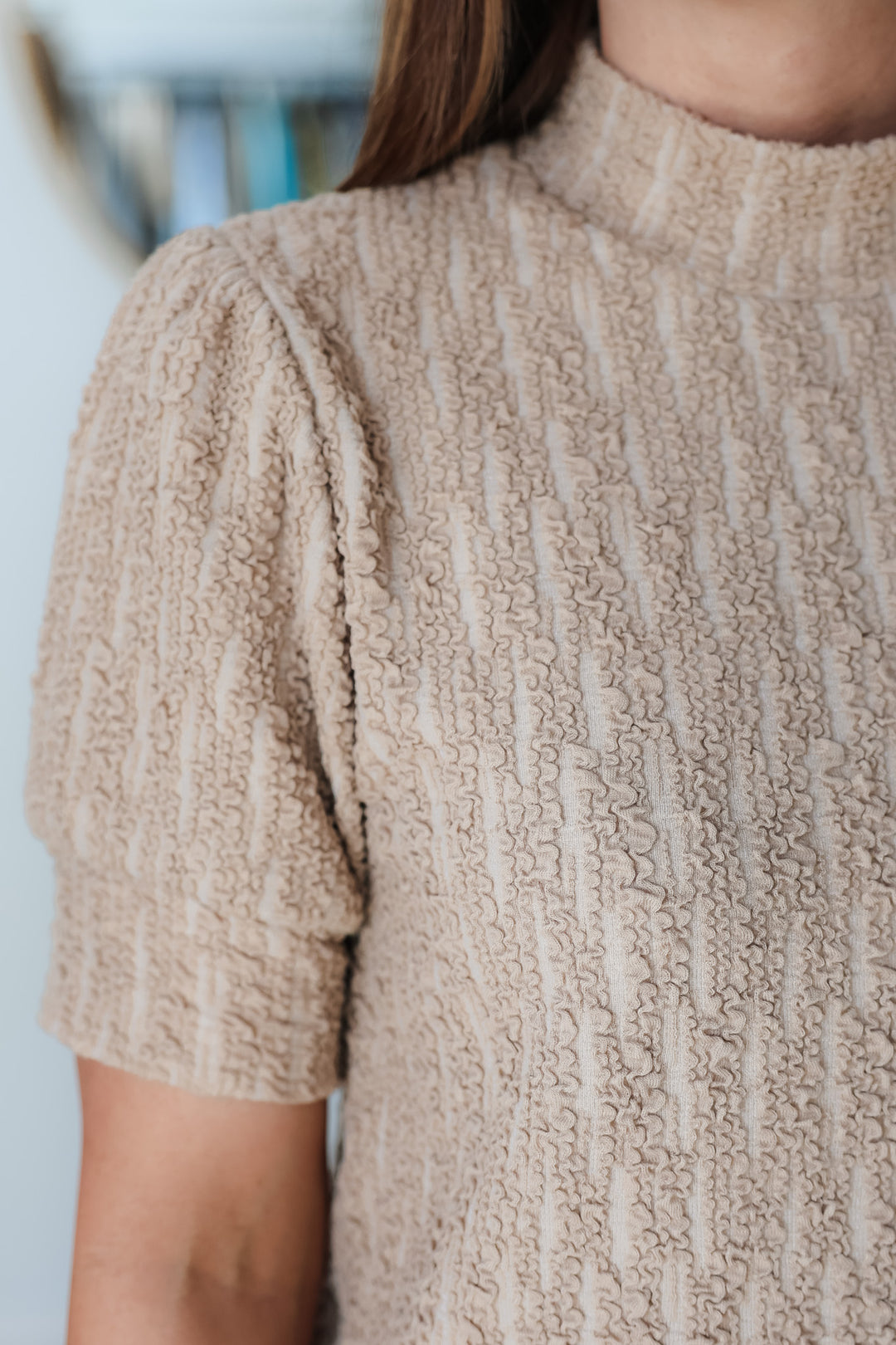 A closeup of the shoulder on a taupe mock neck textured top.