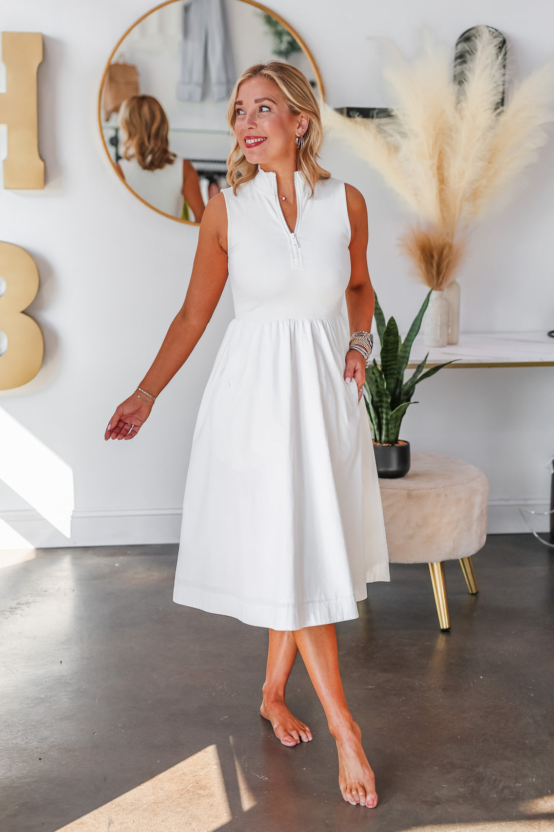 A blonde woman standing in a shop wearing a white dress with a zip collar closure and nylon skirt.