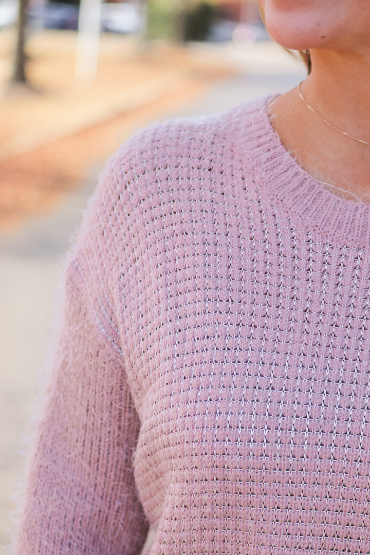 A closeup of the shoulder of a woman wearing a mauve colored sweater.