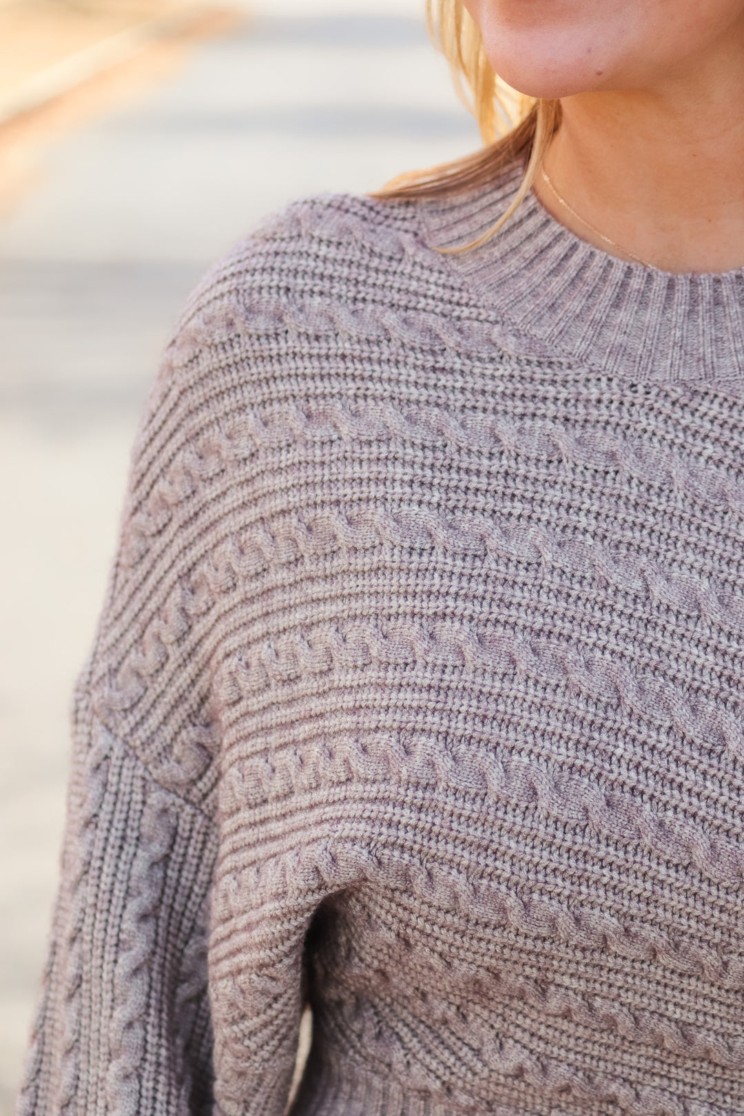 A closeup of the shoulder of a woman wearing a taupe colored cable knit sweater.