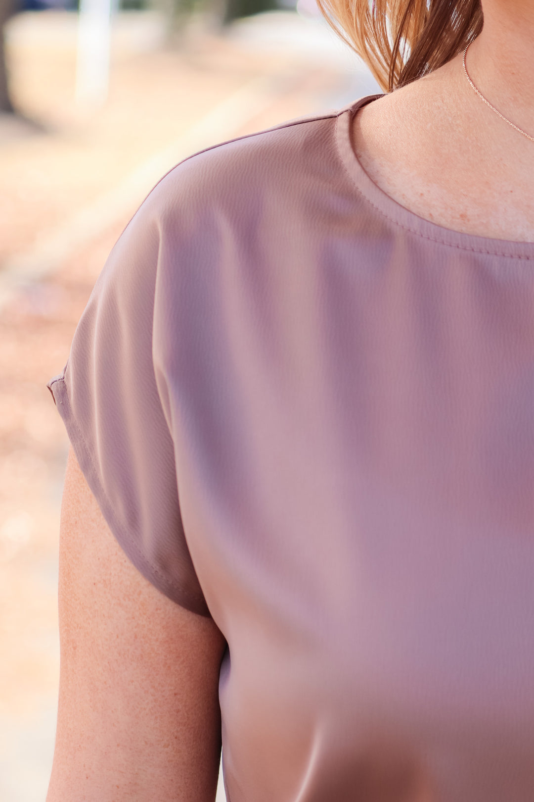 A closeup of the shoulder of a woman wearing a coffee colored satin top with cap sleeves.
