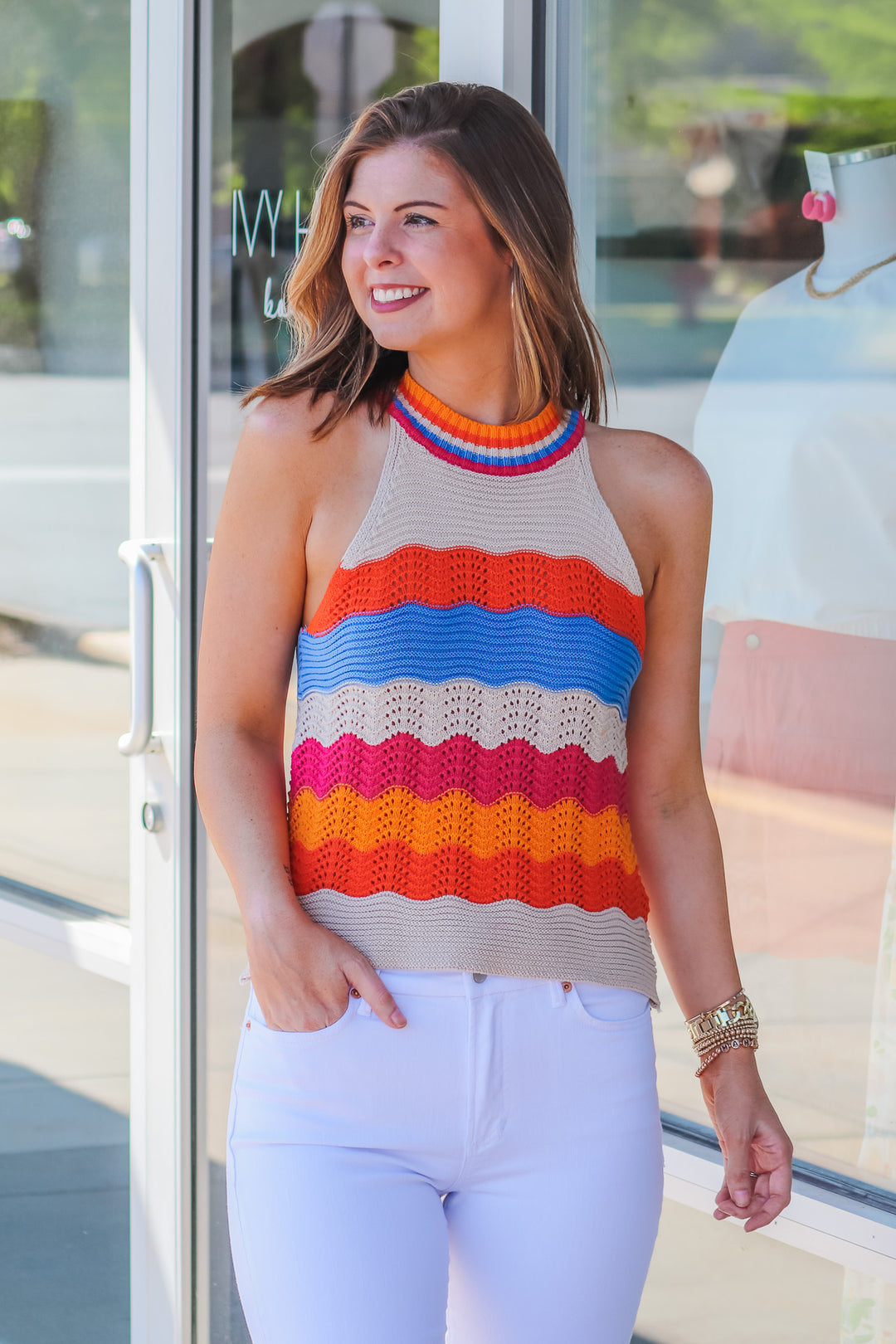 Brunette girl wearing a striped crochet halter top standing in front of a store with her hand in her pocket.