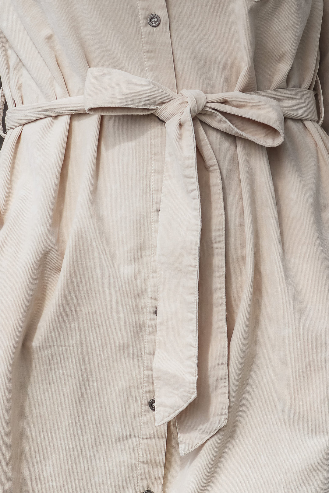 A closeup of the tie belt tied in a bow on a tan corduroy shirt dress.