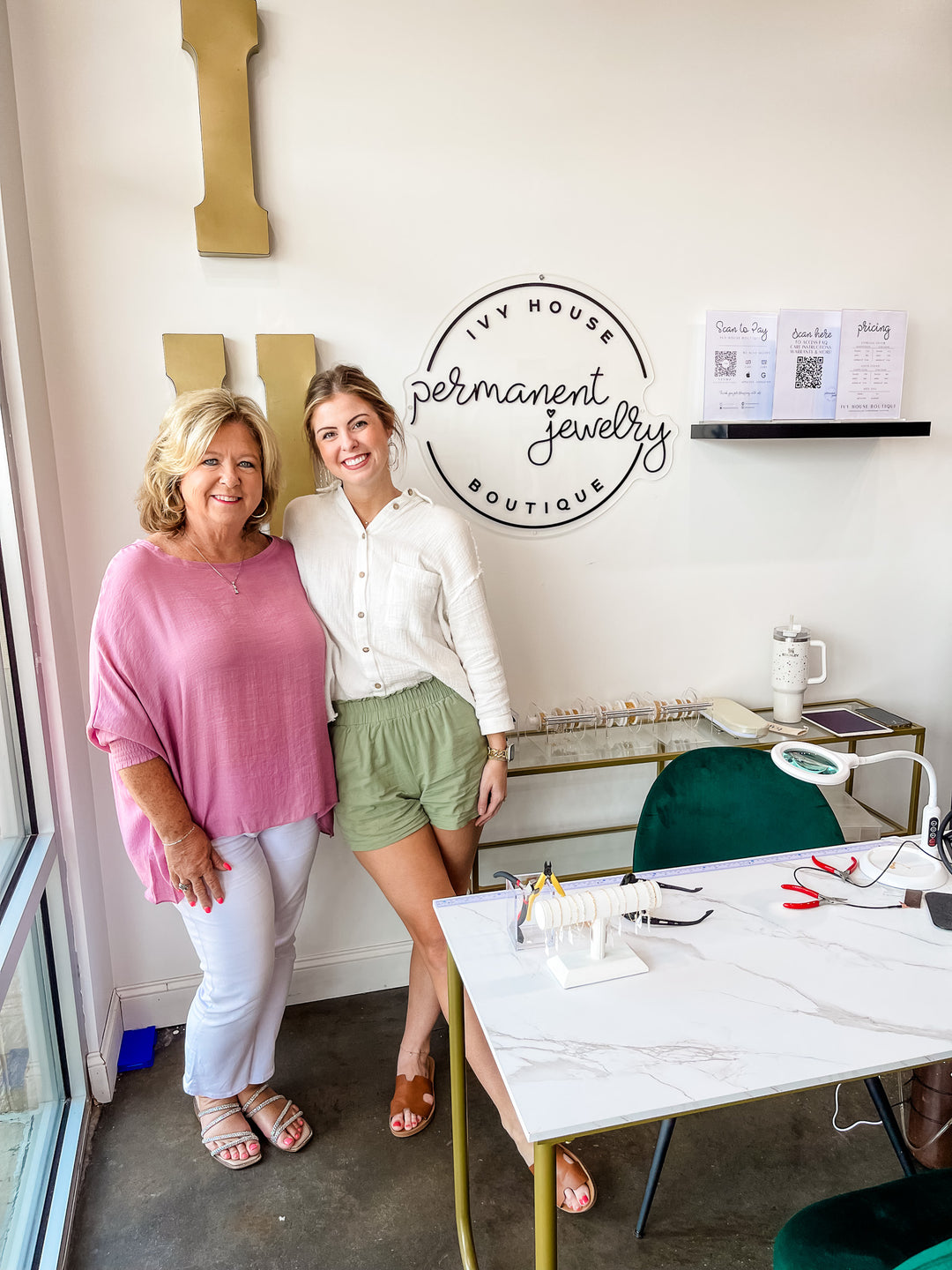 Mom and daughter stand behind a table with permanent jewelry supplies inside of Ivy House Boutique.