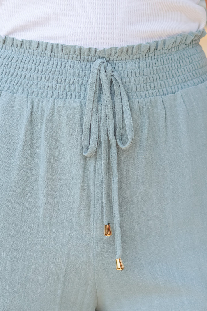 A closeup of the elastic waistband on sage colored linen pants.