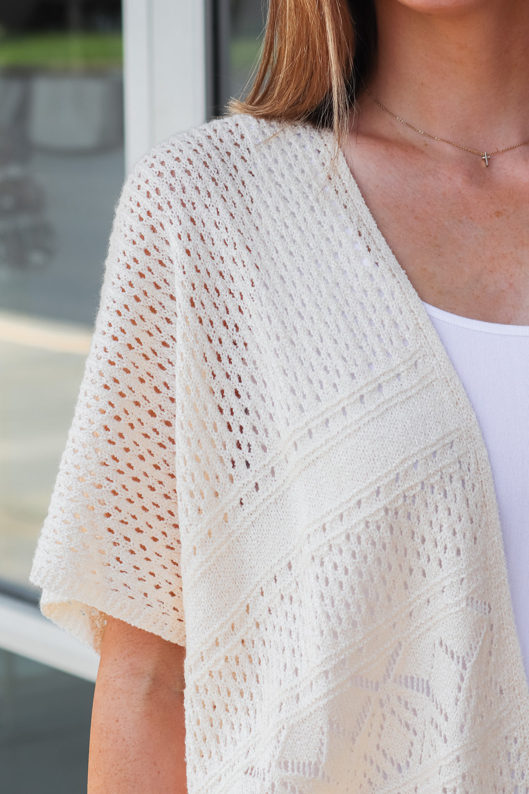 A closeup of a woman wearing a cream colored crochet sweater.