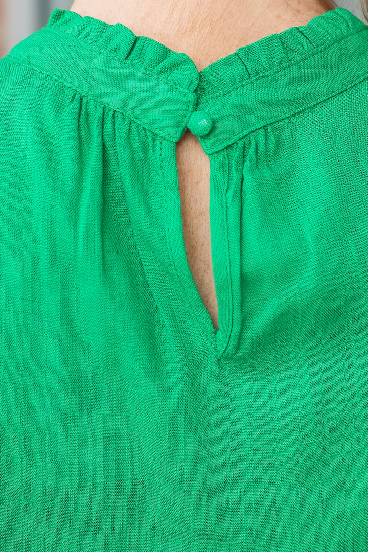 A close up photo of the button closure on the back of a Kelly green shirt.