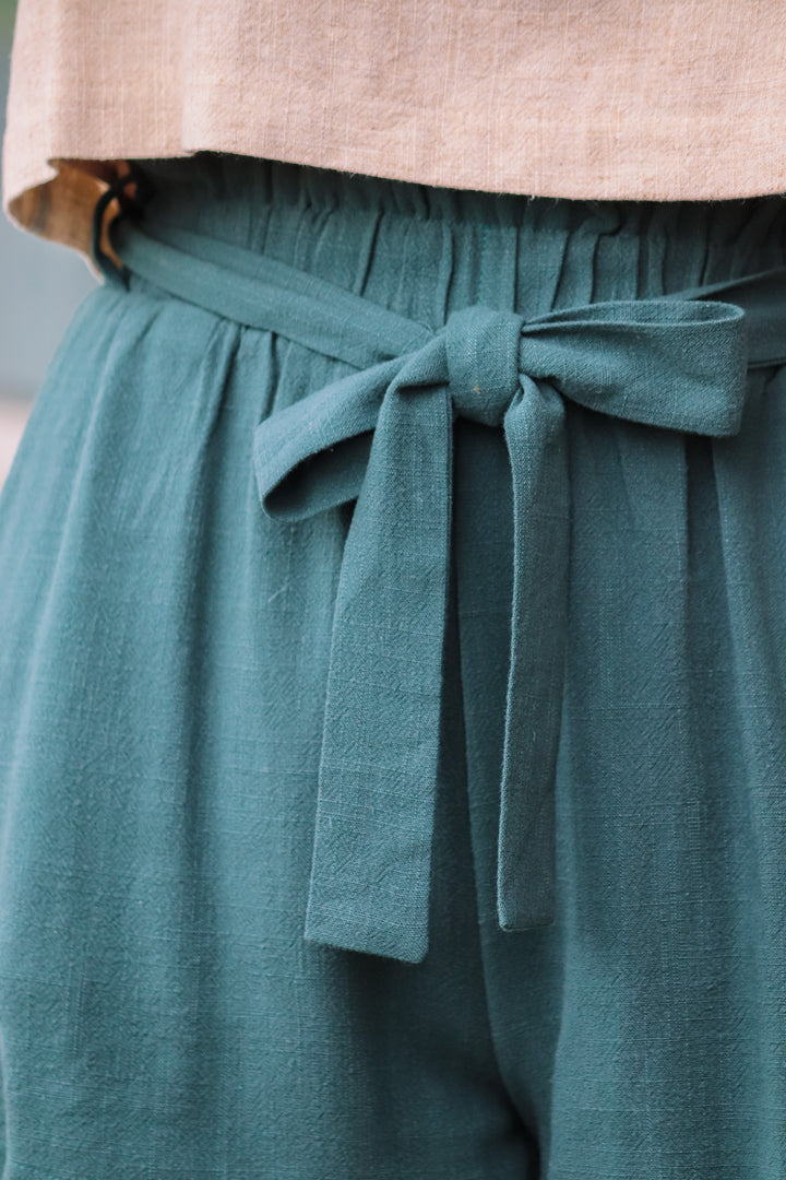 A closeup of the tie belt and elastic waist on the green linen shorts.