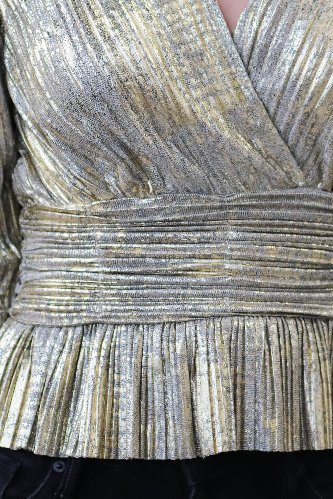 A closeup of the waistband of a metallic gold pleated top.
