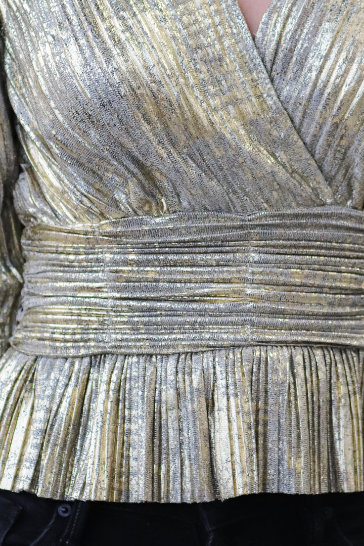 A closeup of the waistband of a metallic gold pleated top.
