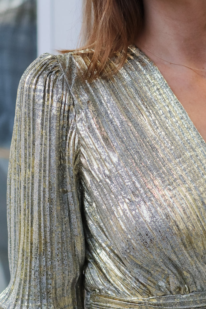 A closeup of the shoulder of a woman wearing a metallic gold pleated top with a v neck.