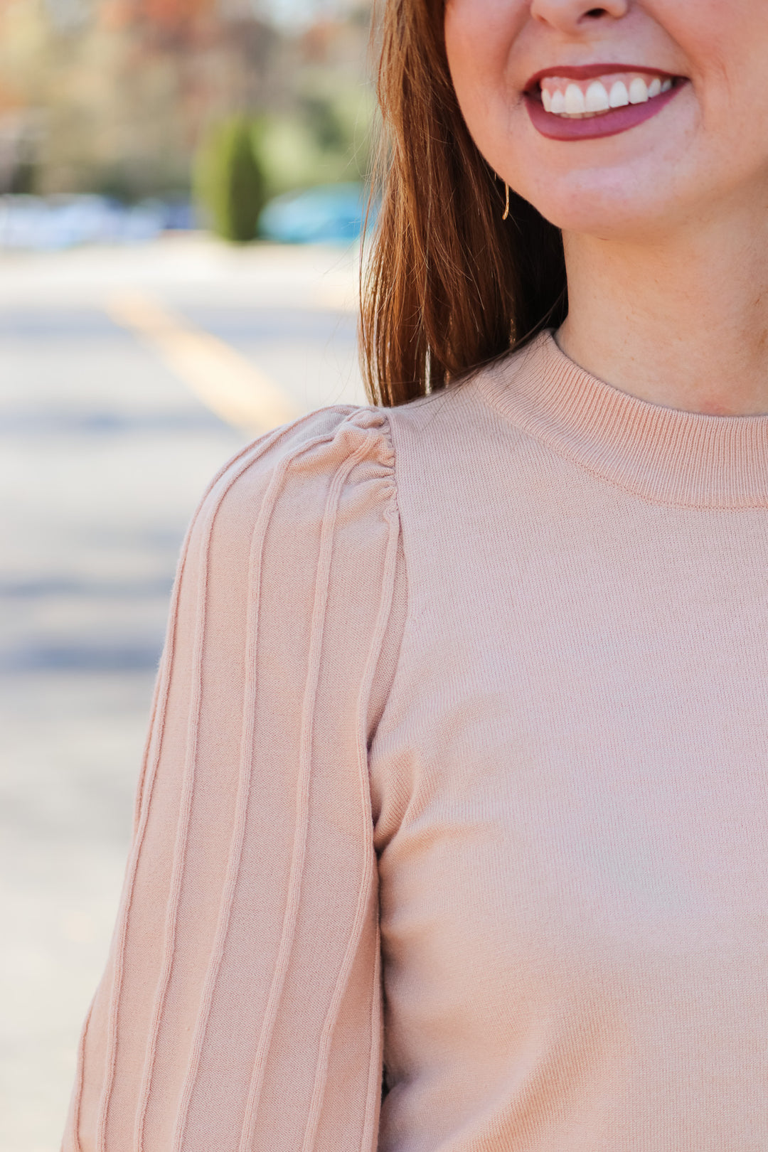 A closeup of the shoulder of a woman wearing an oat colored detailed long sleeve sweater.