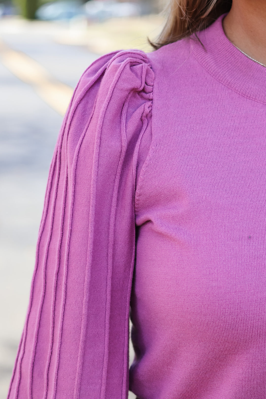 A closeup of the shoulder of a woman wearing a pink detailed long sleeve sweater.