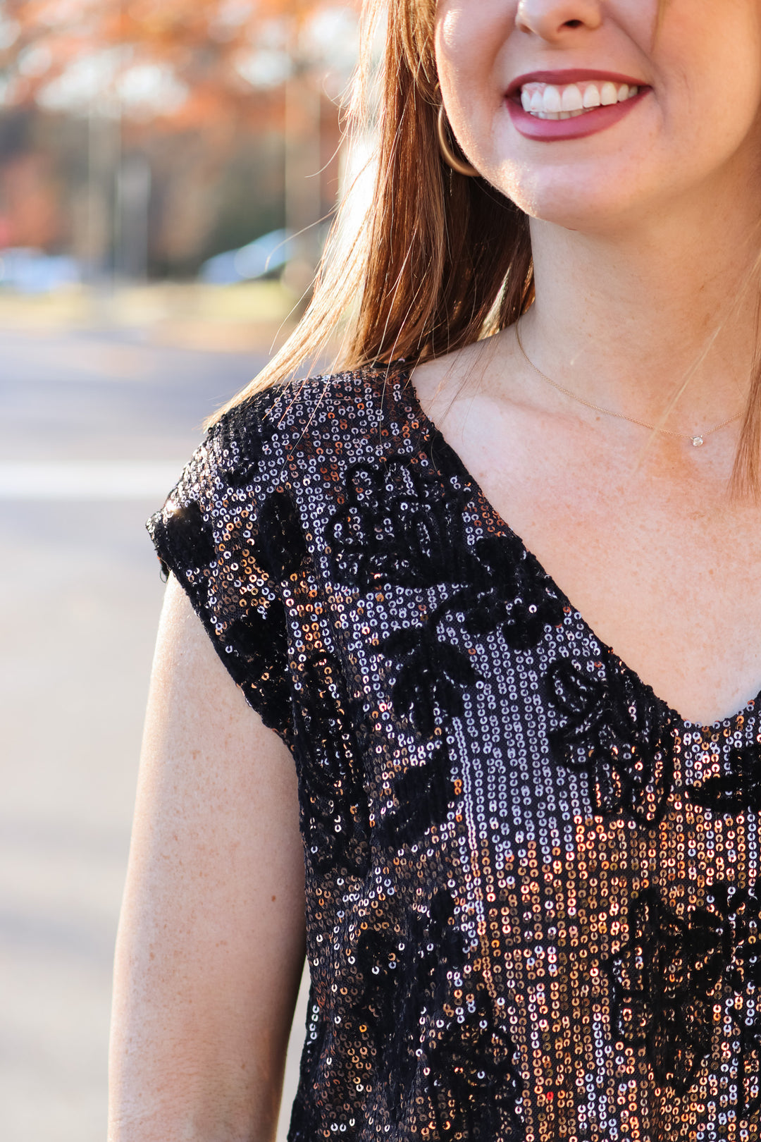 A closeup of the shoulder of a woman wearing a cap sleeve rose gold and black sequin top.