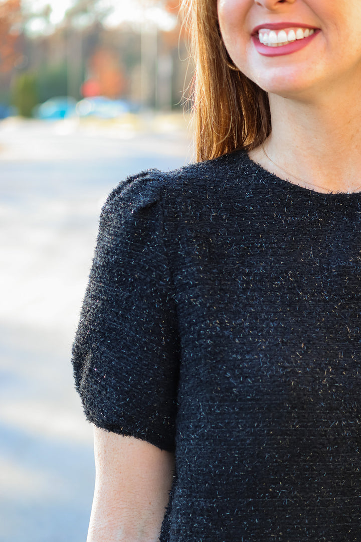 A closeup of the shoulder of a woman wearing a soft and shiny black top with short bubble sleeves.