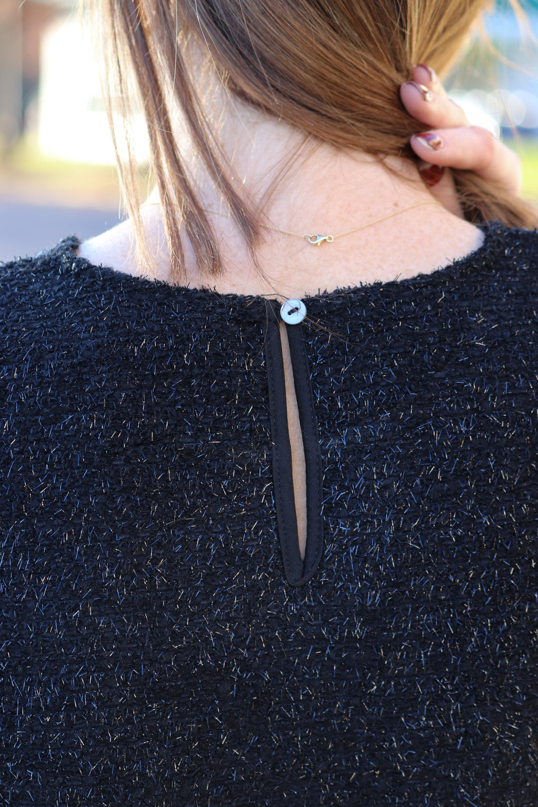 A closeup of the button closure on the back of a soft and shiny top with short bubble sleeves.