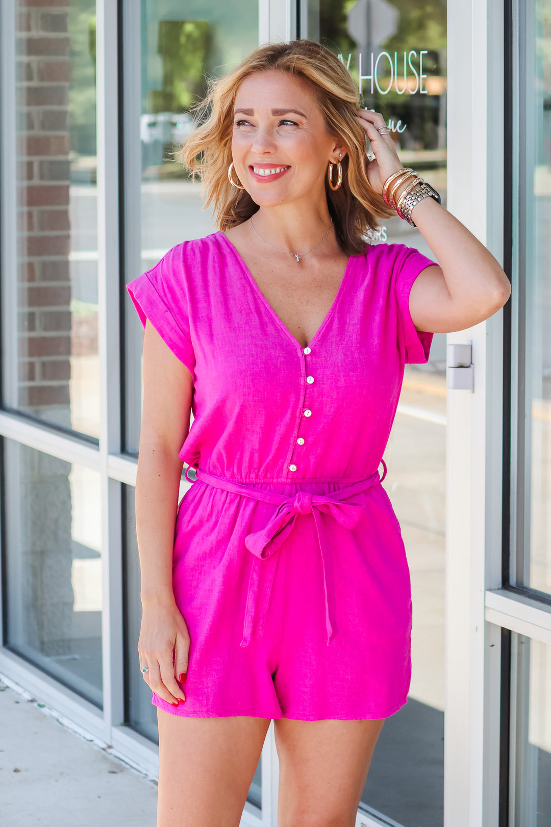 Blonde girl wearing a hot pink romper with a belt tied into a bow. It has 5 buttons on top and short sleeves.  