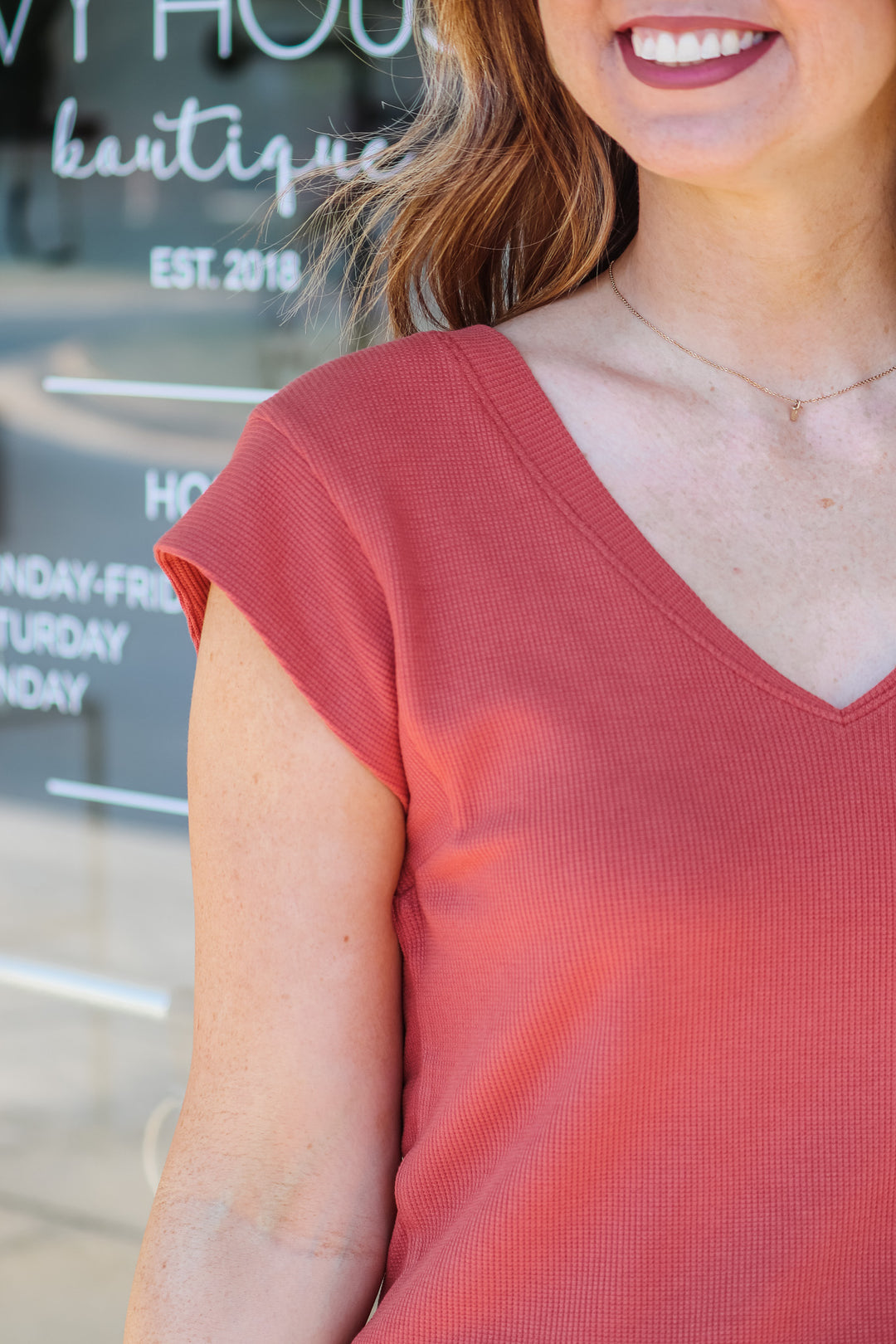 A close up of a woman's shoulder wearing a red clay colored top.