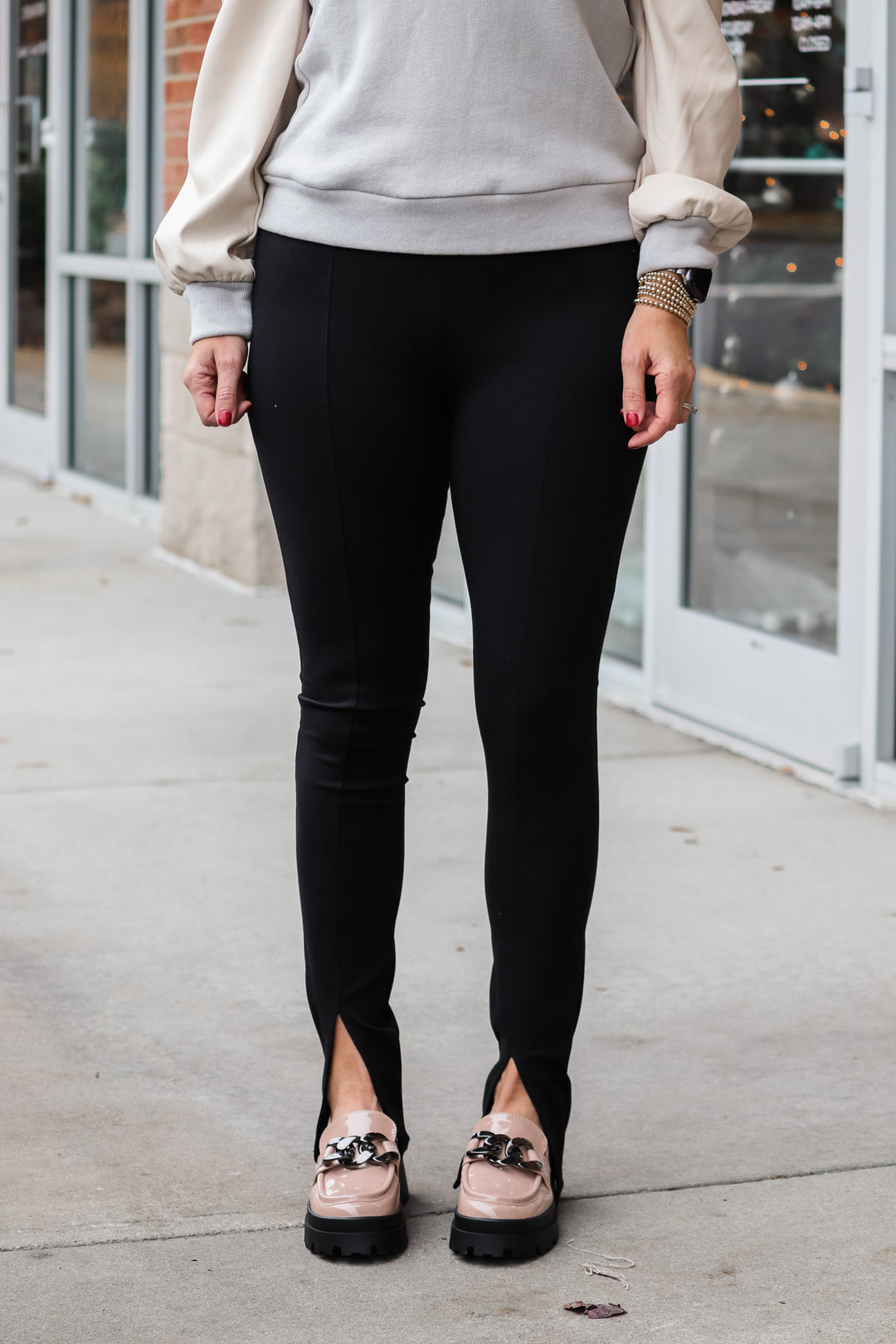 A woman standing in front of a shop wearing black front slit hem leggings and a neutral top.